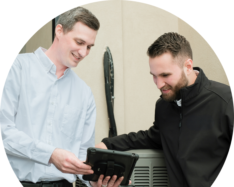 A The Comfort Group technician in a white shirt shows service details on a tablet to a smiling client in a black jacket, standing beside an AC unit outside a beige building. A The Comfort Group technician in a white shirt shows service details on a tablet to a smiling client in a black jacket, standing beside an AC unit outside a beige building.