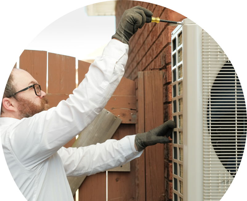 The Comfort Group service personnel working on an AC condenser, using a screwdriver to secure the unit's panel outdoors beside a wooden fence.