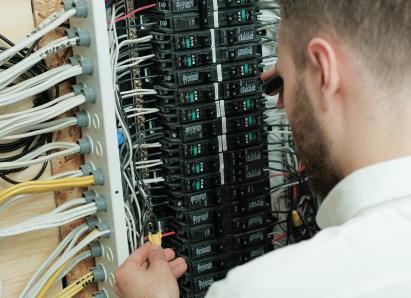 The Comfort Group electrical technician examining wiring connections inside a circuit breaker panel for a residential service check. The Comfort Group electrical technician examining wiring connections inside a circuit breaker panel for a residential service check.