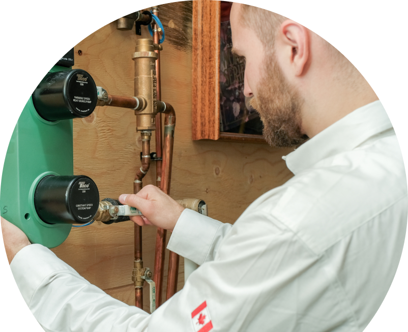 The Comfort Group HVAC specialist performing boiler installation, securing a valve on a new hydronic heating system with copper piping and a green circulation pump mounted on a wooden wall. The Comfort Group HVAC specialist performing boiler installation, securing a valve on a new hydronic heating system with copper piping and a green circulation pump mounted on a wooden wall.