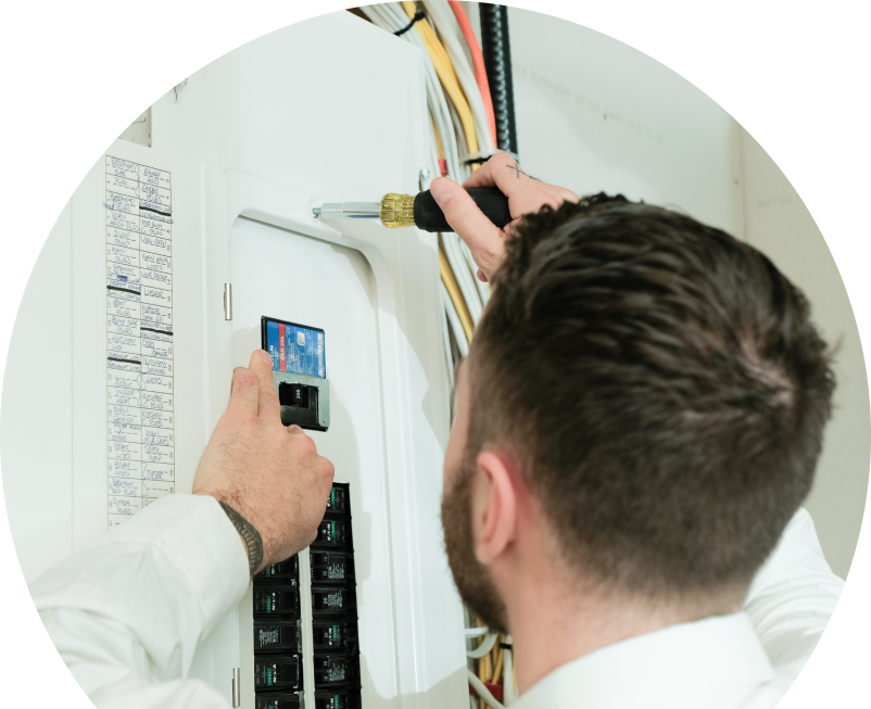 The Comfort Group electrician using a screwdriver to perform an electrical panel upgrade, working near organized wiring in a residential wall. The Comfort Group electrician using a screwdriver to perform an electrical panel upgrade, working near organized wiring in a residential wall.
