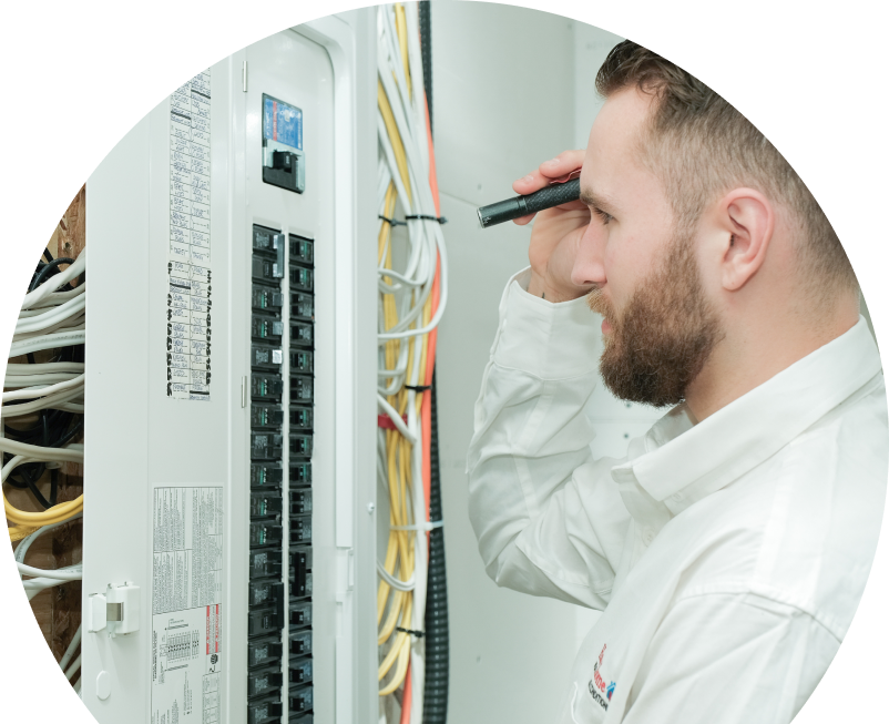 The Comfort Group electrician inspecting residential electrical panel wiring with a flashlight, checking connections and circuit labels. The Comfort Group electrician inspecting residential electrical panel wiring with a flashlight, checking connections and circuit labels.