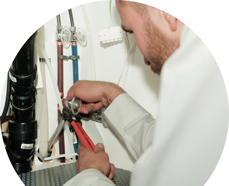 The Comfort Group plumbing expert tightening connections under a sink during a faucet installation, surrounded by hot and cold water supply lines and PVC drainage. The Comfort Group plumbing expert tightening connections under a sink during a faucet installation, surrounded by hot and cold water supply lines and PVC drainage.