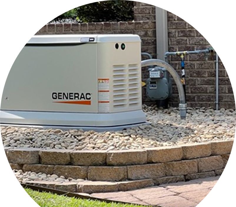 Generac standby generator installed by The Comfort Group on a raised stone platform beside a brick wall, connected to a natural gas meter for backup power supply.