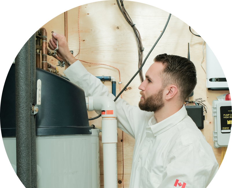 The Comfort Group water heater specialist adjusts piping on a large residential unit during a repair service, with exposed wood paneling and mounted utility components in the background.