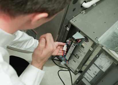 A The Comfort Group heating technician inspecting internal wiring during a service check on a residential heating unit. A The Comfort Group heating technician inspecting internal wiring during a service check on a residential heating unit.