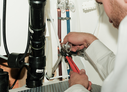 Using two pipe wrenches, a The Comfort Group professional plumber services a pipe connection near a vertical flue or vent pipe. Using two pipe wrenches, a The Comfort Group professional plumber services a pipe connection near a vertical flue or vent pipe.