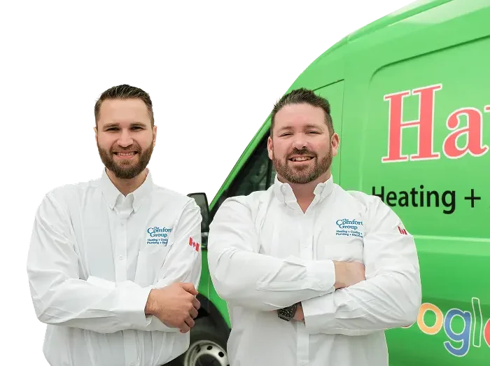 Two The Comfort Group technicians smiling in front of their green service van, wearing issued jackets during an on-site consultation.