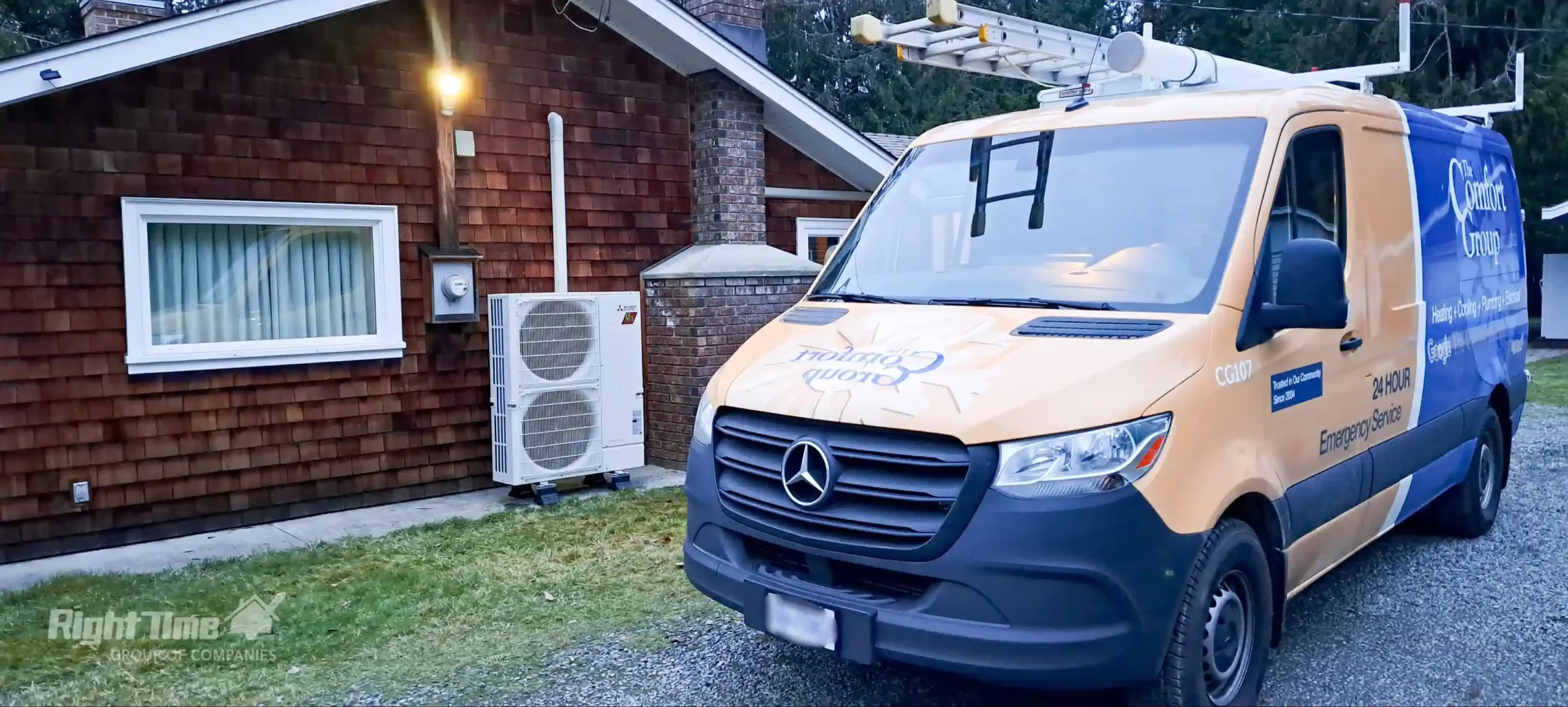 The Comfort Group service van parked beside a home with a Mitsubishi outdoor condenser/heat pump unit on a rainy day.